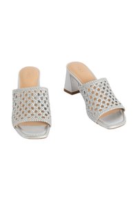 Le mule con tacco argento presentano una tomaia intrecciata con ampi ritagli, punta quadrata e un tacco spesso con una finitura lucida. Soletta beige chiaro.