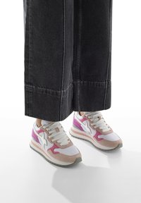 Sneaker con una toma bianca, dettagli rosa e lilla, e una texture in morbido camoscio. Suola in gomma con un design stratificato, abbinate a pantaloni larghi scuri.