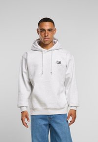 Grauer Hoodie aus weichem Stoff mit einer vorderen Kängurutasche, verstellbarem Kapuzenzug und einem kleinen gestickten Logo auf der Brust.