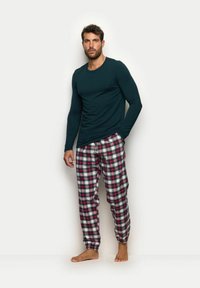 Langärmliges dunkelgrünes Oberteil, kombiniert mit karierter Hose in Rot, Weiß und Navy. Aus Baumwollmaterial, lockerer Schnitt, mit elastischen Bündchen und Taillenbund.