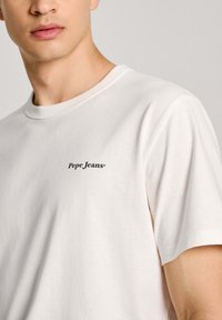 Baltos medvilnės marškinėliai su apvalia iškirpte ir trumpomis rankovėmis. Turi subtilų tamsiai mėlyną logotipą "Pepe Jeans" kairėje krūtinės vietoje.