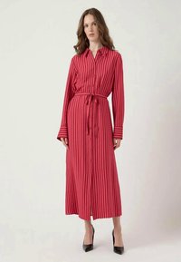 Vestido button-up de riscas rosas longas com uma cintura ceifeada, mangas longas e um silhueta fluida. Usado com saltos altos pretos.