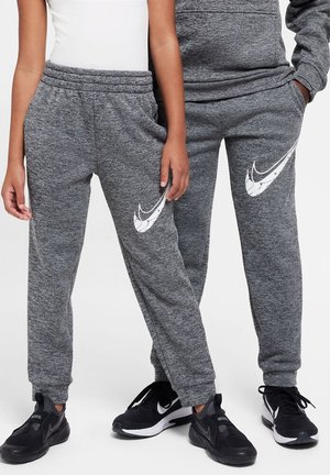 Twee personen in bijpassende grijze Nike trainingsbroeken en zwarte Nike sneakers staan zij aan zij, met hun handen ontspannen langs hun lichaam.