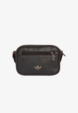 Pieni musta nahkainen olkalaukku, jossa etutasku vetoketjulla ja beigenvärinen Adidas trefoil -logo keskellä edessä.