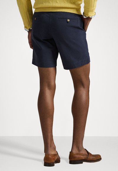 Șorturi bleumarin din amestec de bumbac, cu două buzunare la spate ce au nasturi aurii. Purtați cu un pulover galben și mocasini maro.