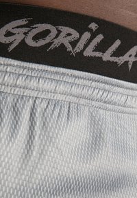 Grijze sportshorts hebben een gestructureerd oppervlak en een zwarte elastische tailleband met het woord "GORILLA" prominent weergegeven in grijze letters.