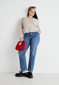 Beige knit sweater, light blue straight-leg jeans, black platform shoes, and a red textured handbag. Hair tied with a pink bandana.
