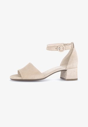 Sandale en daim beige avec bout ouvert, bride à la cheville et talon bloc. Présente une texture lisse et un détail de boucle ajustable.