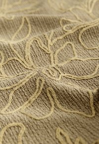 Tessuto beige con una trama a rilievo decorato con un motivo floreale di un giallo chiaro, caratterizzato da una superficie ondulata per un aspetto tattile.