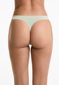 Lichtgroene stringonderbroek met een gladde textuur en minimale bedekking. Dunne tailleband en naadloos ontwerp voor comfort.