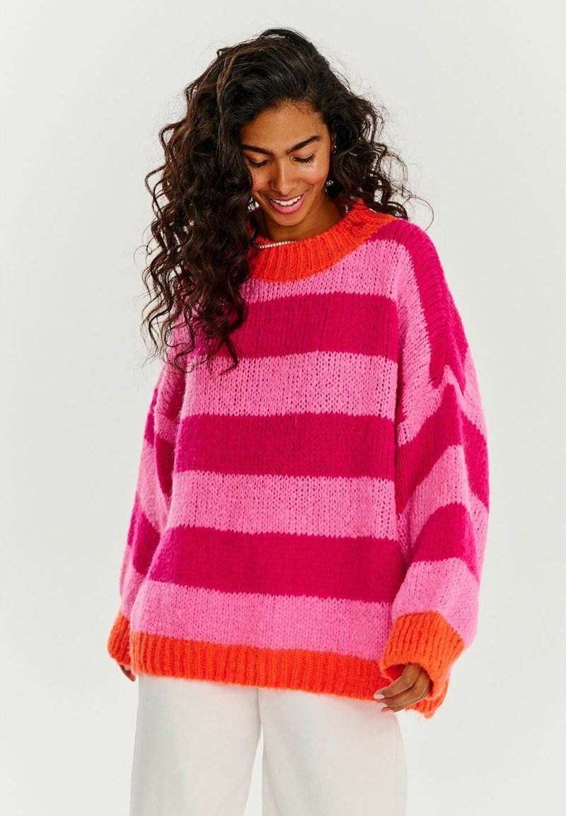 Pletený svetr s širokými horizontálními pruhy v jasně růžové, světle růžové a oranžové barvě, s ribbovaným oranžovým výstřihem a nadměrnými rukávy.