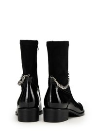 Czarne botki za kostkę z błyszczącej lakierowanej skóry, teksturowanym zamszowym wierzchem, niskim obcasem w kształcie bloku oraz srebrnym łańcuszkiem po boku.