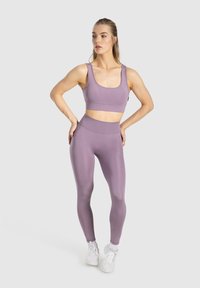 Fioletowy stanik sportowy i legginsy z wysokim stanem wykonane z elastycznej tkaniny, charakteryzujące się gładką teksturą i dopasowanym krojem, w zestawieniu z białymi sneakersami.