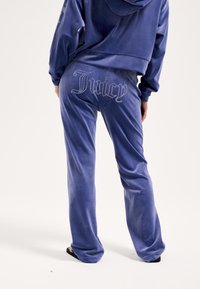 Aksamitny dres w głębokim niebieskim kolorze, z krótkiem kapturem i dopasowanymi spodniami. Na tylnej części zdobienie z kryształków tworzy napis "Juicy".