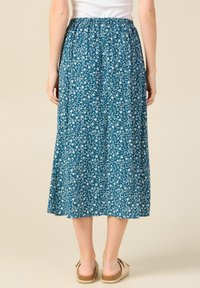 Teal midi-hame, jossa on valkoinen kukkakuosi, kerätty vyötärö ja kevyitä kankaita. Yhdistetty vaaleisiin espadrille-sandaaleihin.