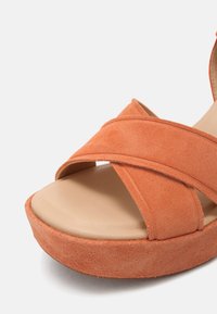 Sandales en daim orange avec des brides croisées et une semelle plateforme. La semelle intérieure beige lisse contraste avec l'extérieur orange texturé.