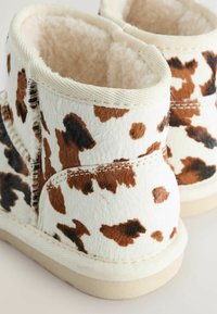Stivaletti alla caviglia con stampa in pelle di mucca bianca e marrone, con interno morbido, cuciture a vista e suola in gomma beige. Finitura testurizzata simile ai peli.