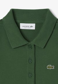 Grünes geripptes Poloshirt in schmaler Passform, ausgestattet mit einem klassischen Kragen und einer drei-Knopf-Leiste. Auffälliges gesticktes Logo auf der Brust.