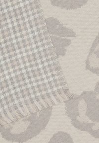 Tissu tissé gris présentant un motif à carreaux d'un côté et un design de feuilles subtil de l'autre, avec des bords effilochés.