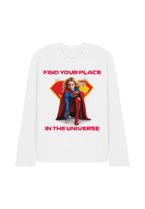 Kind, verkleidet als Supergirl, kniet mit rotem Umhang vor einem gelben und roten Emblem, auf dem weißen Shirt steht "Find your place in the universe".