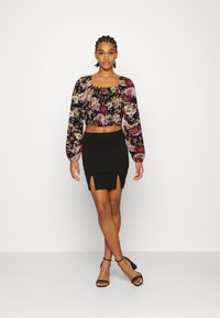 Blusa floral cropped com mangas longas e decote quadrado, combinada com uma saia mini preta com fendas laterais e design ajustado.