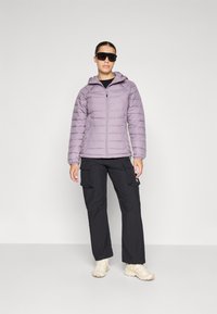 Lyse lilla pufferjakke med hette, glidelås og quiltet mønster, kombinert med svarte cargo-bukser og beige sneakers.