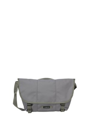 Graue Timbuk2 Umhängetasche mit verstellbarem Schultergurt, Frontklappe, zwei Schnallenverschlüssen und Markenlabel vorne in der Mitte.