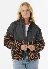 Chaqueta de forro polar con sección superior de nylon negro y sección inferior con estampado animal en naranja. Presenta un cierre con cremallera en la parte delantera y un pequeño bolsillo en el pecho.