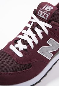 Sneaker atletica bordeaux in materiali mesh e suede, con lacci bianchi, logo "N" grigio e colletto imbottito, dotata di suola in gomma.