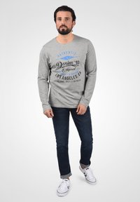 Langærmet grå T-shirt med trykt tekst, parret med mørkeblå jeans og hvide sneakers. Flad tekstur, casual pasform og rund halsudskæring.