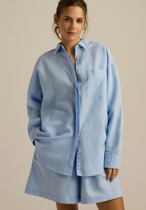 Jasnoniebieska, oversize koszula z guzikami, wykonana z miękkiego materiału, z kieszonką z przodu i luźnym krojem, zestawiona z dopasowanymi szortami.