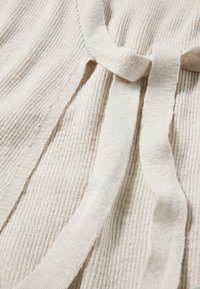 Cardigan in maglia a coste beige con chiusura a cravatta, morbida al tatto, maniche ampie con sottili linee verticali e design aperto davanti.
