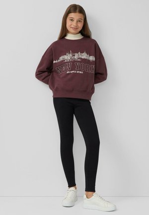 Bordowy sweatshirt z białą grafiką "NEW YORK", w połączeniu z czarnymi leginsami i białymi sneakersami, wyróżniający się luźnym krojem i ściągaczami przy mankietach.