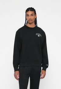 Sweatshirt preto com punhos e barra canelados, apresentando o logo branco "Champion" no lado esquerdo do peito. Feito de um suave material misto de algodão.