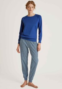 Blauwe sweatshirt met ronde hals en lange mouwen, gecombineerd met joggingsbroek met een patroon in tinten blauw en wit, voorzien van elastische boorden.