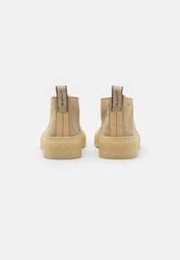 Paire de bottines beige en daim avec des semelles épaisses et texturées, vues de dos, avec des languettes portant la mention GANT.