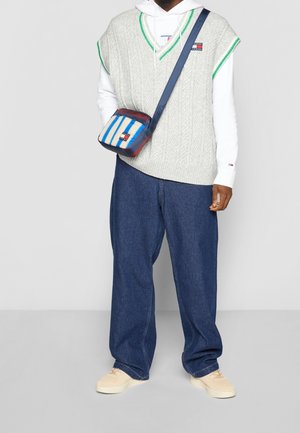 Graue Strickweste mit grünem Akzent über einem weißen Hoodie, kombiniert mit locker sitzenden blauen Denim-Hosen und einer mehrfarbig gestreiften Tasche.