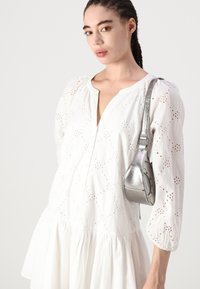 Rochie albă din bumbac, cu detalii din broderie, cu nasturi pe față și fustă amplă. Geantă metalică argintie pe umăr, cu formă curbată și curea ajustabilă.