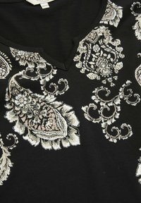 Sort skjorte med intrikate hvide og beige paisleybroderier, V-udskæring og glat stofkvalitet. Mærke synligt indeni.