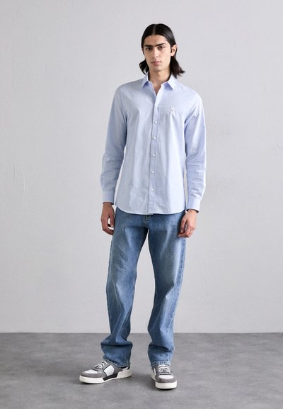 Cămașă butonată de culoare bleu deschis, cu dungi subțiri albe, asortată cu blugi bleu deschis, de tip relaxed-fit și pantofi sport gri cu accente negre și albe.