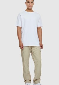 Witte katoenen t-shirt met een ronde hals, gecombineerd met beige cargobroeken met zijzakken. Witte sneakers maken de look af.