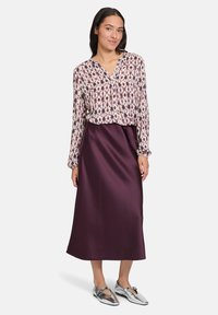 Camicia a maniche lunghe con motivo floreale in rosa e crema, abbinata a una gonna midi in satin bordeaux e scarpe metallizzate argento.