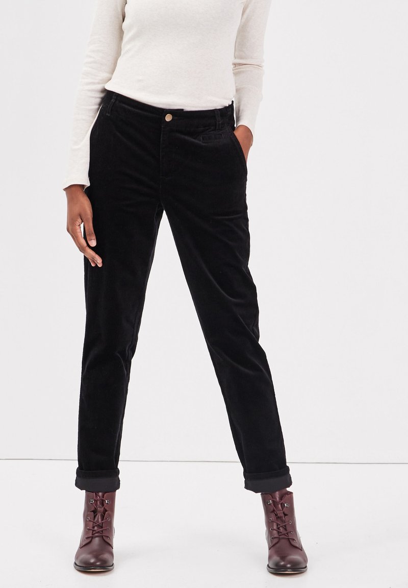 Svarta kordflorsbyxor med rak passform, med framfickor och uppvikta benslut, tillsammans med vinröda snörstövlar.