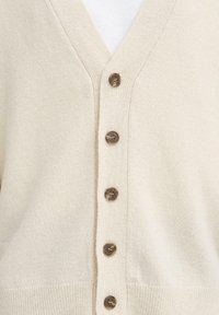 Lys beige cardigan med V-hals og seks mørkebrune knapper foran. Den myke teksturen er synlig og fremhever den koselige utseende.