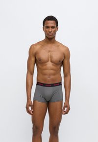 Gray boxer shorts made of stretch fabric with a black waistband featuring the "HUGO" logo in red. Smooth texture and fitted design.