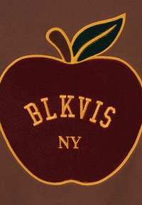 Hnedá látka s motívom bordového jablka so žltým obrysom, textom "BLKVIS NY" v krémovej farbe a zeleným listovým akcentom.