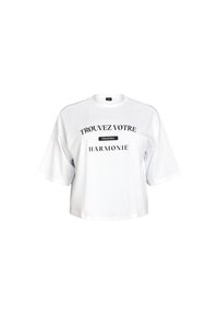 White cotton t-shirt with oversized short sleeves and a round neck. Front features black text: "TROUVEZ VOTRE PROPRE HARMONIE."