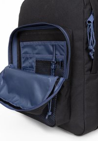 Černý látkový batoh s modrou vnitřní podšívkou, disponující zapínací přední kapsou, síťovými oddíly a nastavitelnými zipovými táhly.