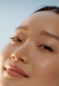 Närbild av ett slätt, ljus hyansikte med framträdande kindben, subtilt glänsande läppar och naturlig makeup; mjukt ljus framhäver ansiktsdragen.