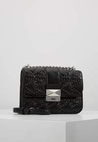 Borsa a tracolla nera trapuntata in pelle, caratterizzata da borchie argentate, chiusura a flap con placca logata metallica e tracolla a catena.